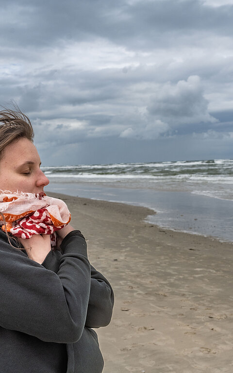 Frau an der Wasserkante am Strand von Juist im Herbst oder Winter