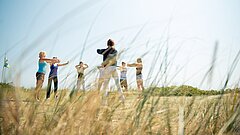 Gruppe an Menschen macht Atemübungen in der Juister Natur in der Nähe des TöwerVital mit Wellnessabteilung