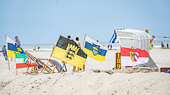 Newsletter von Juist - monatliche Juistpost - Bild vom Strand auf Juist mit Flaggen deutscher Bundesländer an einer Sandburg