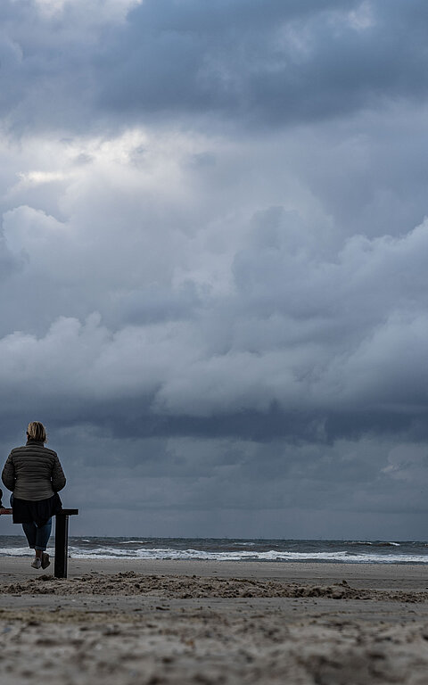 Zwei Personen sitzen bewusst auf einer Bank am Juister Strand unter dunklem Himmel