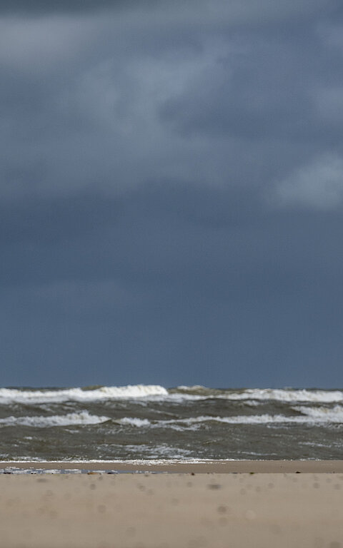 Person im Regenmantel am Juister Strand direkt an der Wasserkante spürt die Thalasso-Wirkung