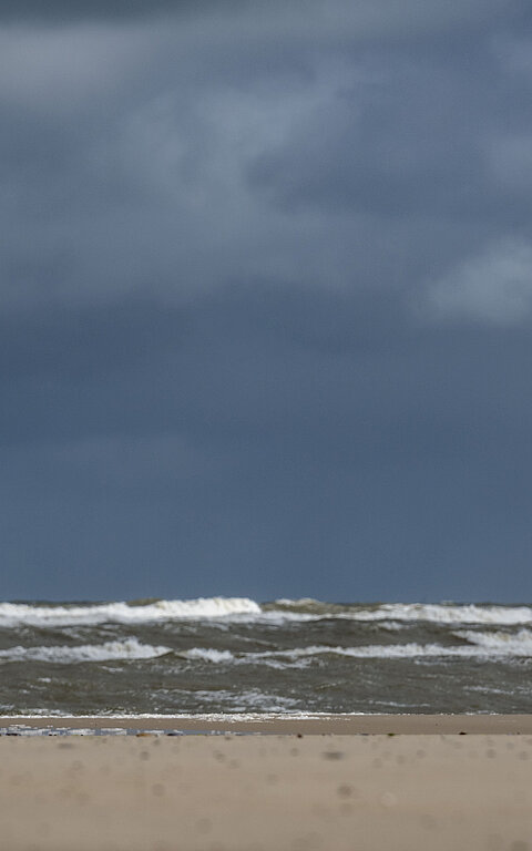 Person im Regenmantel am Juister Strand direkt an der Wasserkante spürt die Thalasso-Wirkung