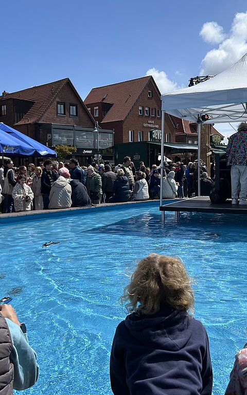Bild zeigt Stimmung auf dem Kurplatz auf Juist beim Juistival mit Kindern und Schiffchenteich sowie Bühne im Schiffchenteich