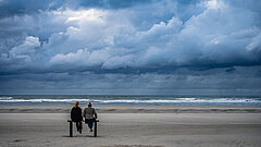Newsletter von Juist - monatliche Juistpost - Bild vom Strand auf Juist mit zwei Personen auf einer Bank an der Wasserkante