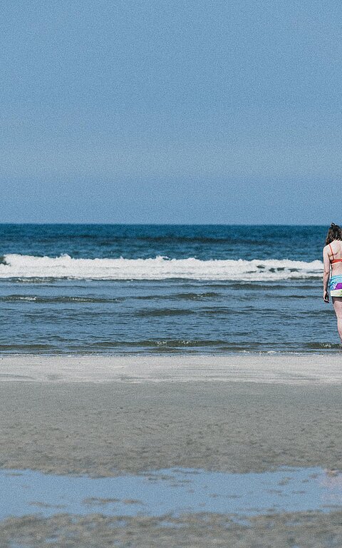 Familie an der Wasserkante der Nordsee auf Juist, zwei Frauen, vermutlich Oma und Mutter, halten ein Kind zwischen sich an den Händen