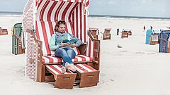Frau liest in einem Strandkorb am Strand auf Juist