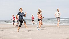 Gruppe beim Strandsport auf Juist mit verschiedenen Gesundheitskursen an der Nordsee, Menschen laufen und ziehen die Knie hoch an die Brust direkt an der Wasserkante