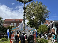 Bild zeigt Stimmung auf dem Kurplatz auf Juist beim Juistival feiernden Menschen mit Sicht auf die Bühne über Menschen mit Maibaum und Merchandising-Zelt