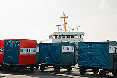 Anreise mit der Fähre auf die Nordseeinsel Juist - Bild zeigt Gepäckcontainer(blau und rot) im Hafen von Juist, dahinter das Oberdeck mit Masten einer Inselfähre