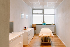 Wellnessangebote auf Juist - Foto zeigt Behandlungsraum im TöwerVital Wellnesszentrum auf Juist mit einer Liege und großen Fenstern sowie heller Einrichtung
