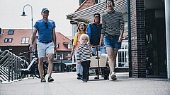 Anreise nach Juist mit Gepäck zu Fuß im Ort, Bild zeigt eine Familie mit Handkarren im Ort auf der Strandstraße, ein Kind vorneweg