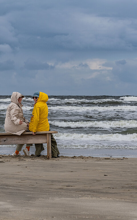 Herbsturlaub auf Juist - zwei Personen in Jacken am Strand auf Juist vor den Wellen an der Wasserkante