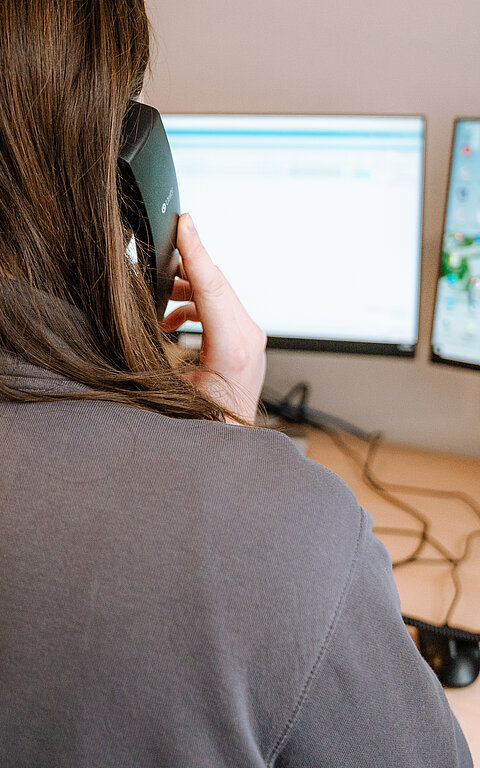 Tourist-Information im Rathaus auf Juist - Bild zeigt eine Angestellte von hinten am Telefon, vor ihr auf dem Schreibtisch zwei Monitore