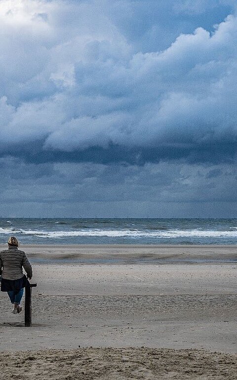 Zwei Personen auf einer Bank am Juister Strand mit beeindruckendem Himmel, Horizont und Nordsee
