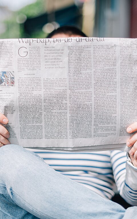 Mann liest eine Zeitung auf einer Parkbank