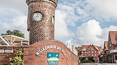 Alter Bahnhof auf Juist am Ortseingang mit Willkommens-Schild, Ensemble aus Gebäuden aus rotem Klinker mit Straße am rechten Bildschirmrand